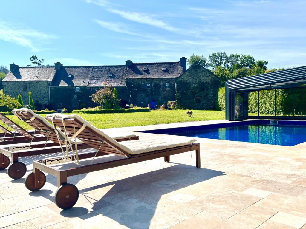 Sun Loungers in foreground with blue swimming pool, green lawn with a springer spaniel and 17th Century Gites in the background in Brittany
