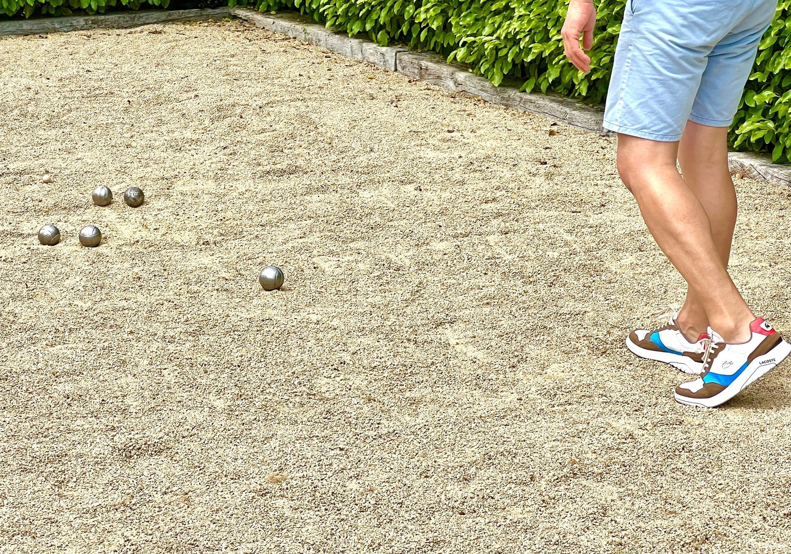 Brittany Holiday Cottages with Heated Swimming Pool and Private Petanque Pitch Man in Blue Shorts playing Petanque on a sandy Boules Pitch with stainless stell boules